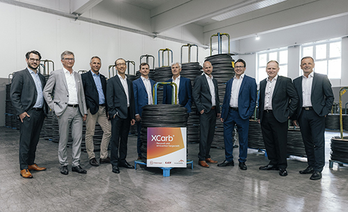 The dream teams of ArcelorMittal (headed by Uwe Braun), Finkernagel (with Timo Finkernagel) and EJOT (Markus Rathmann) standing together close to the XCarb® recycled and renewably produced coils